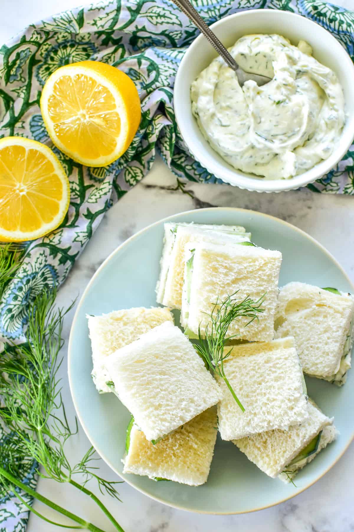 Overhead image of Cucumber Sandwiches on a light blue plate with fresh lemons