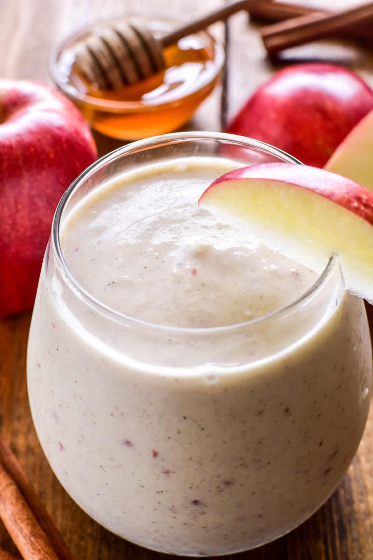 Close up of Apple Smoothie in a glass with fresh apples, cinnamon sticks, and honey
